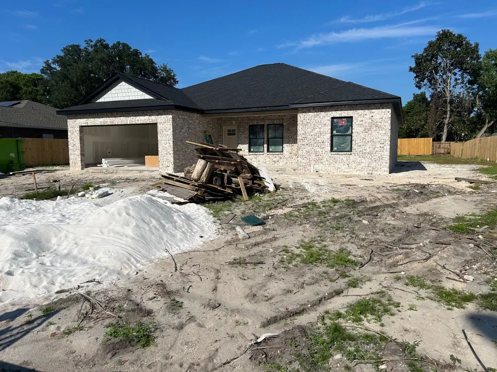A pile of framing lumber, pallets and tree stumps in front of a new brick house